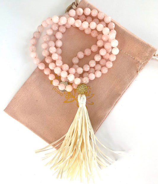 Coiled rose quartz mala with a cream raffia tassel resting on a blush pouch