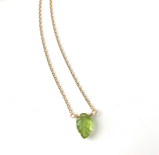 Carved peridot leaf pendant on a delicate gold filled chain against white