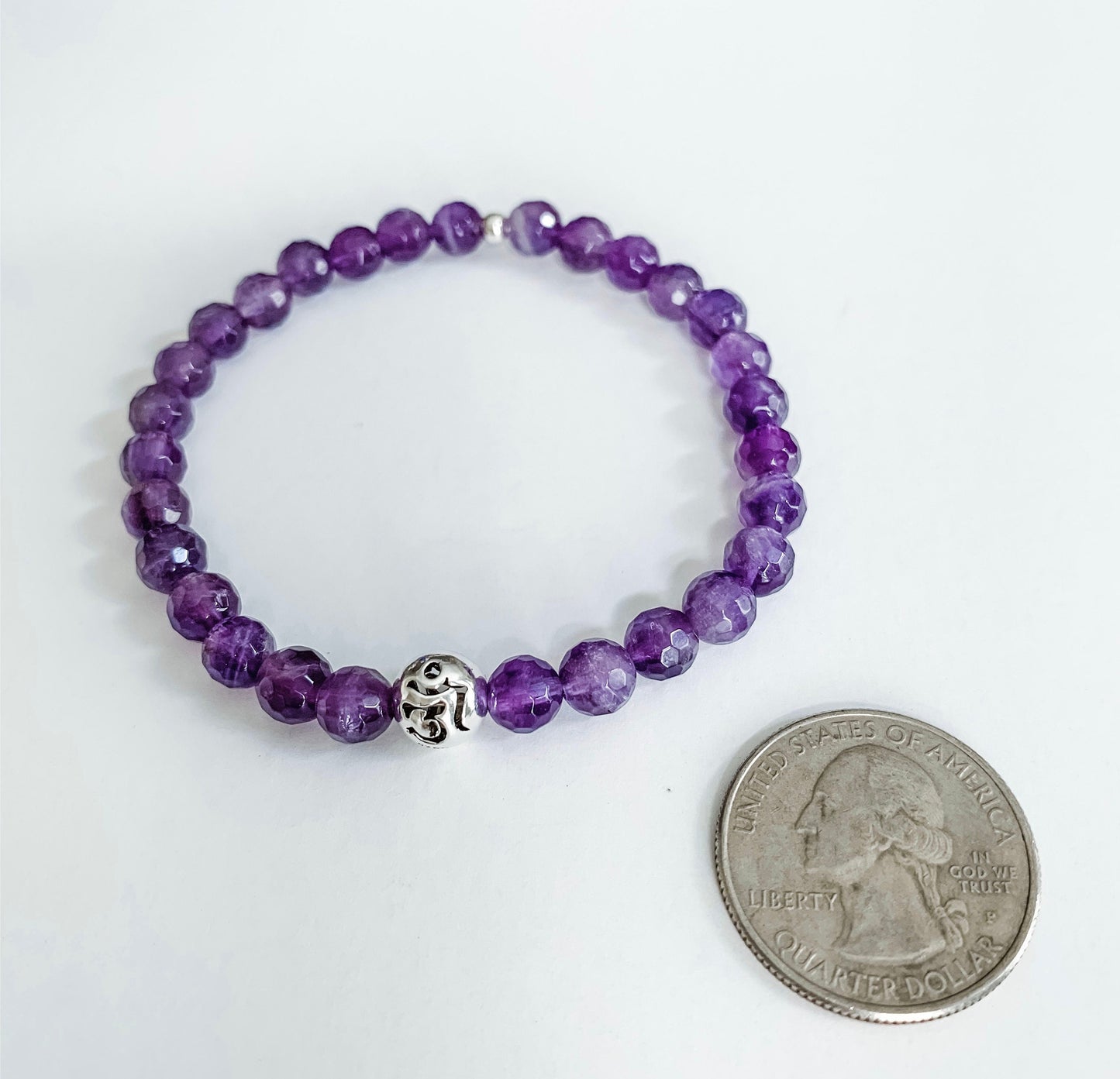 Amethyst beaded bracelet with sterling silver Om round ball bead charm next to a quarter for size comparison