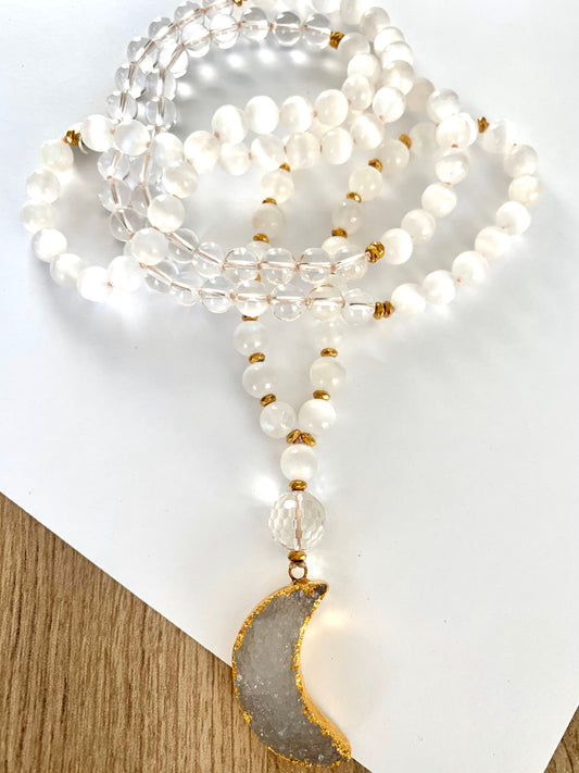 Coiled selenite and clear quartz mala on wood with a gold rimmed druzy crescent moon pendant