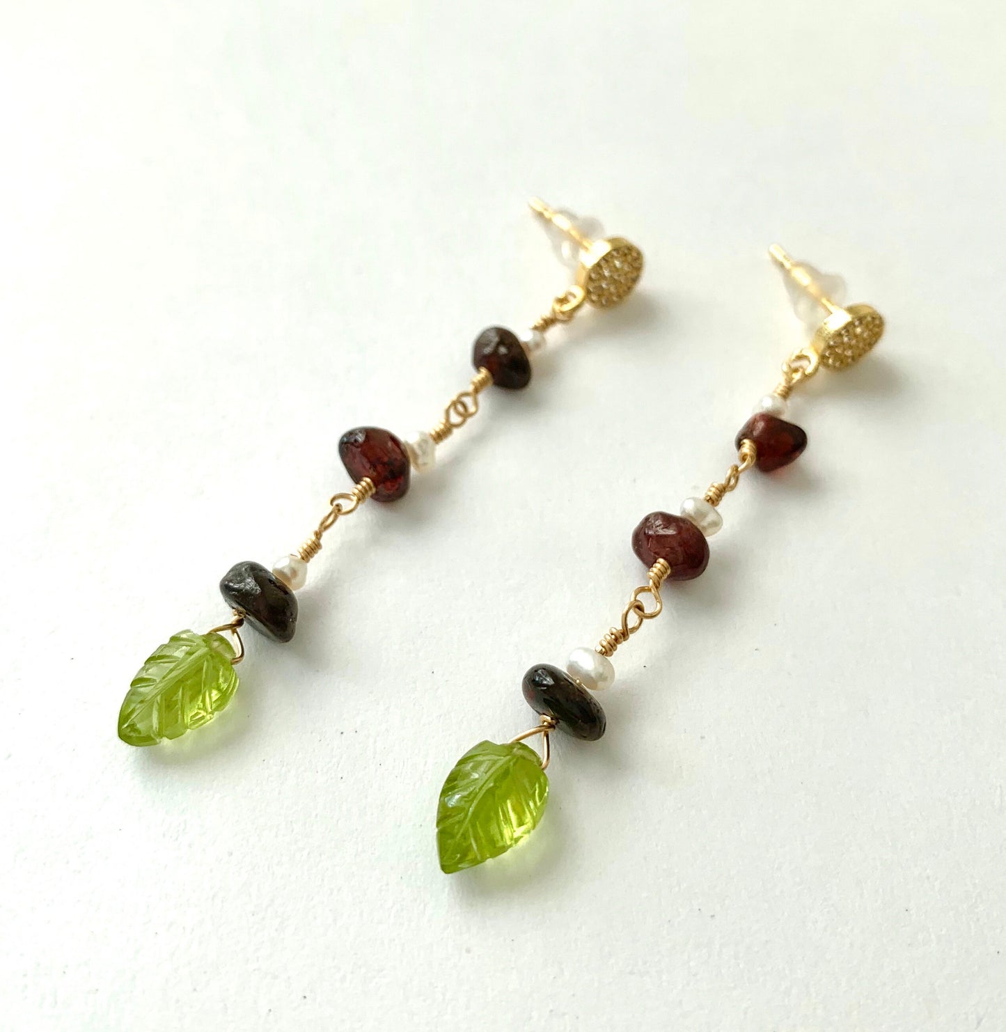 yellow gold filled dangle earring with pave' cz round studs and 3 garnet and pearl stations suspended from chain. carved peridot leaves hang from the bottom.  