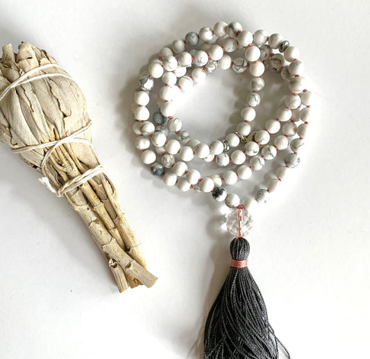 Coiled white howlite mala with a charcoal tassel beside a white sage smudge bundle