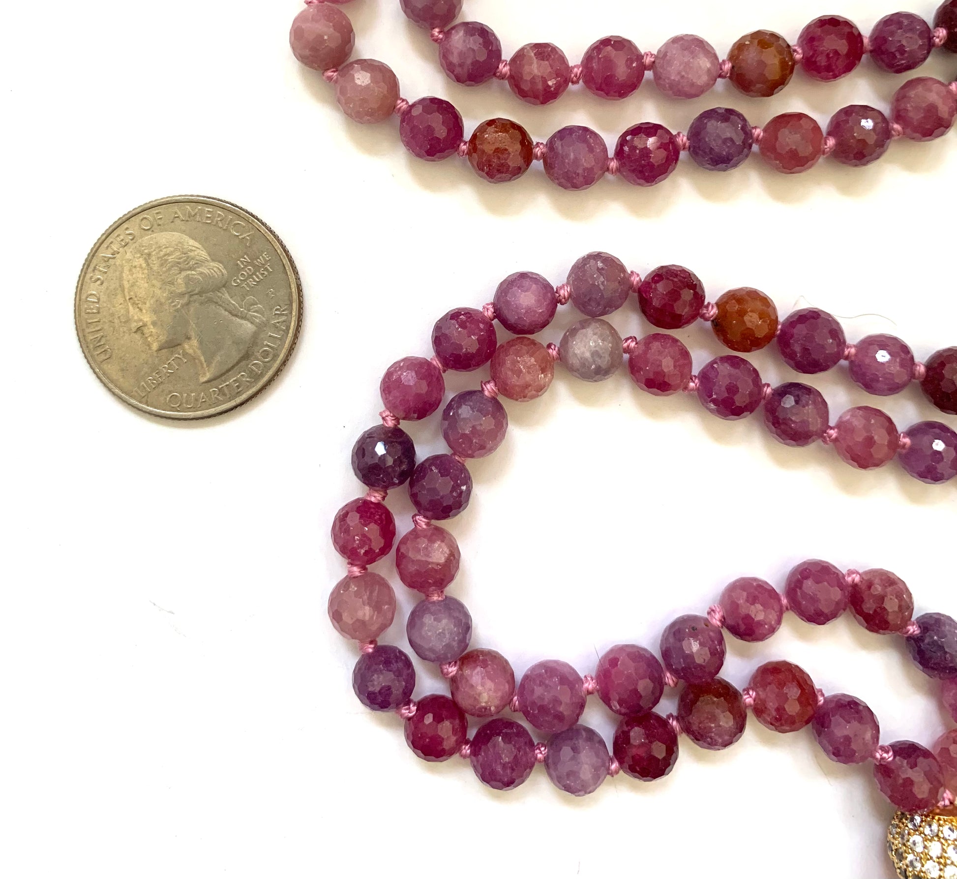 close up of ruby mala beads next to a quarter for size comparison