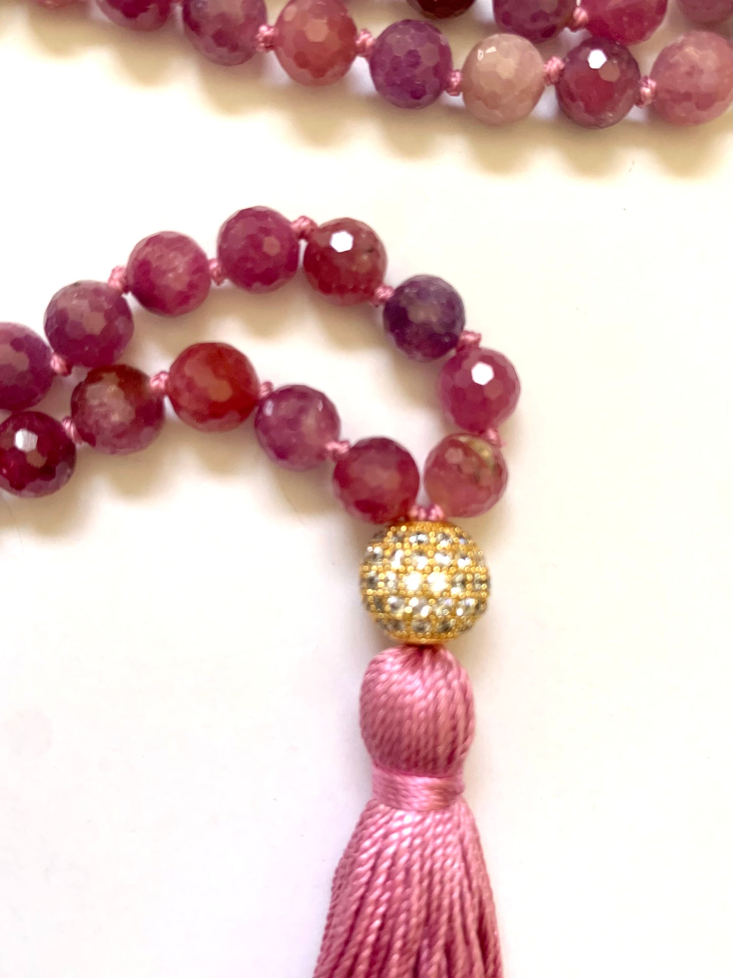 Close up of Ruby mala beads, 6mm, knotted on pink silk, pink silk tassel, pave cz gold toned guru bead